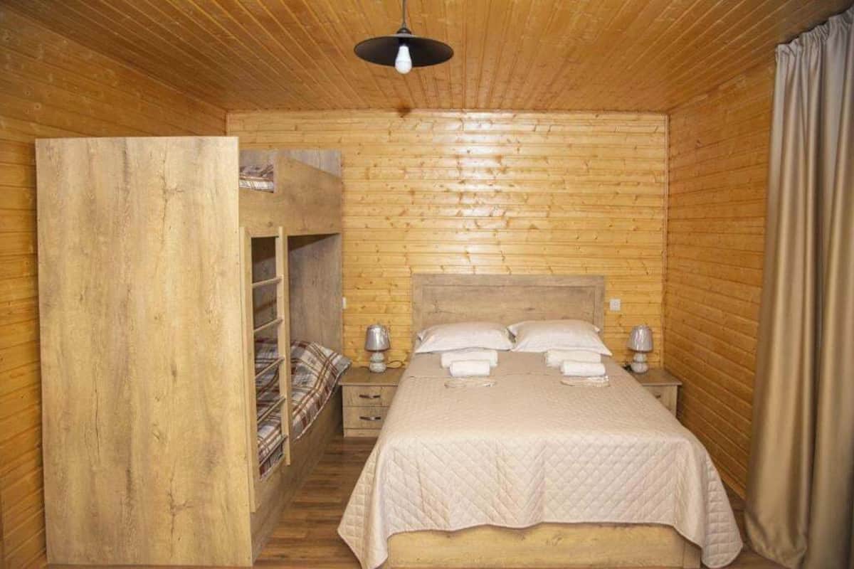 A wooden cabin-style room with a bunk bed, a bedside table with a lamp, and a hanging light fixture.