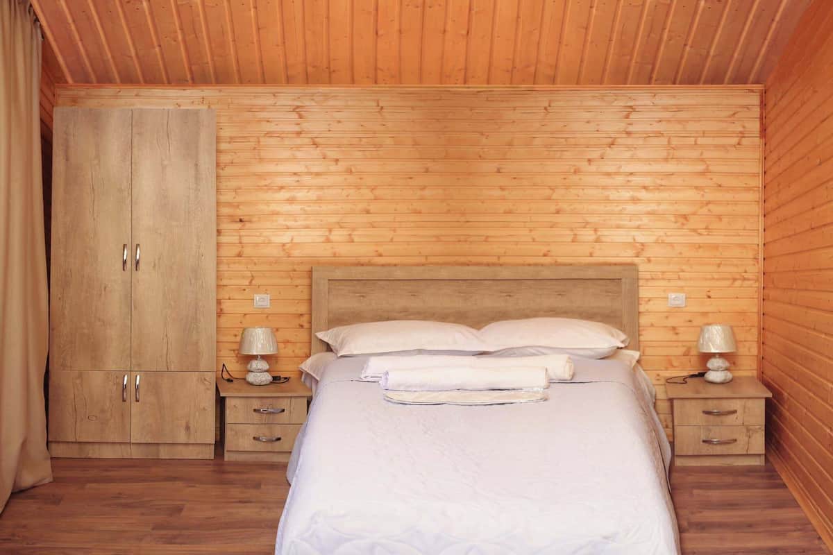 A bedroom with a wooden headboard, a bed with white linens, two bedside tables with lamps, and a wooden wardrobe.