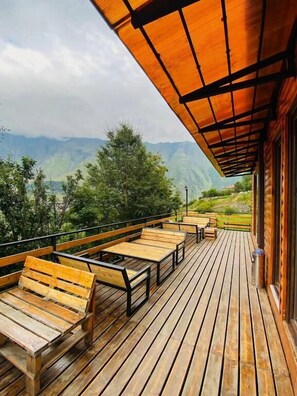 Una terraza de madera con bancos y un área cubierta que da a un paisaje montañoso.
