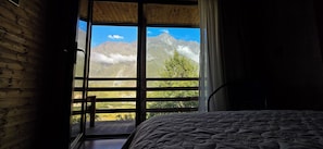 Une chambre avec un lit, une fenêtre donnant sur les montagnes et une porte en bois.