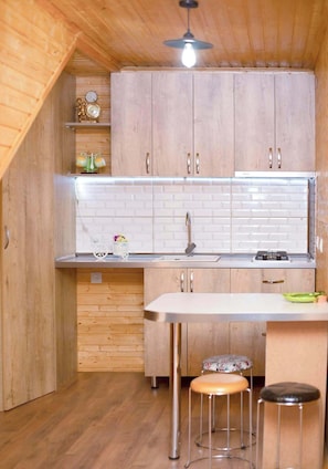 A compact kitchen with wooden cabinets, a white countertop, a sink, and a small stool.