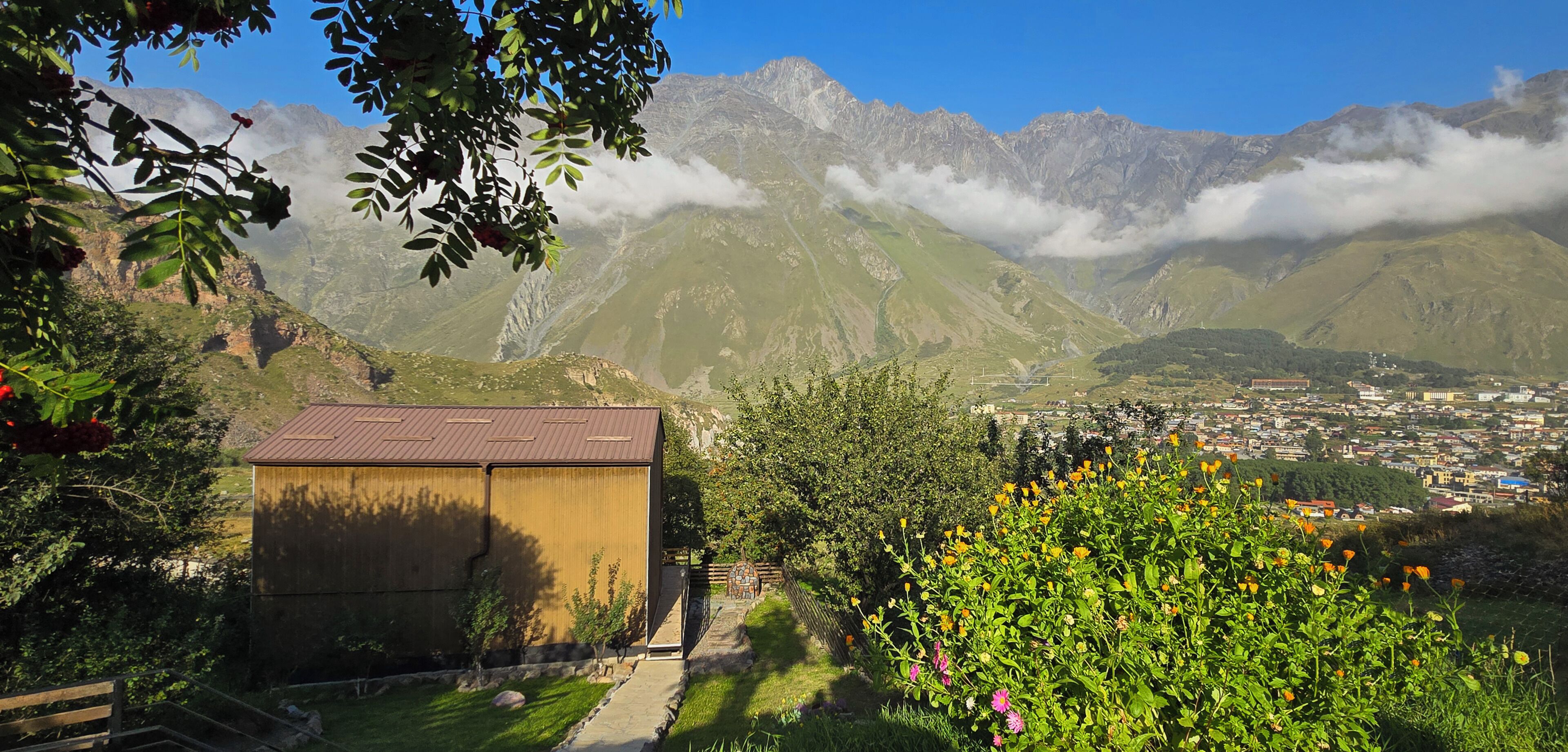 A mountain landscape with a small building, a town in the valley, and a clear sky.
