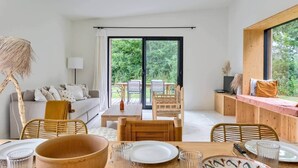 A modern interior with a dining area, sofa, and a view through a glass door to an outdoor space. - Casa Sitha magnifique maison de vacances de 110m2 (Gouville-sur-Mer)