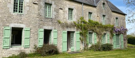 A stone building with green shutters, a grassy lawn, and a clear sky.
