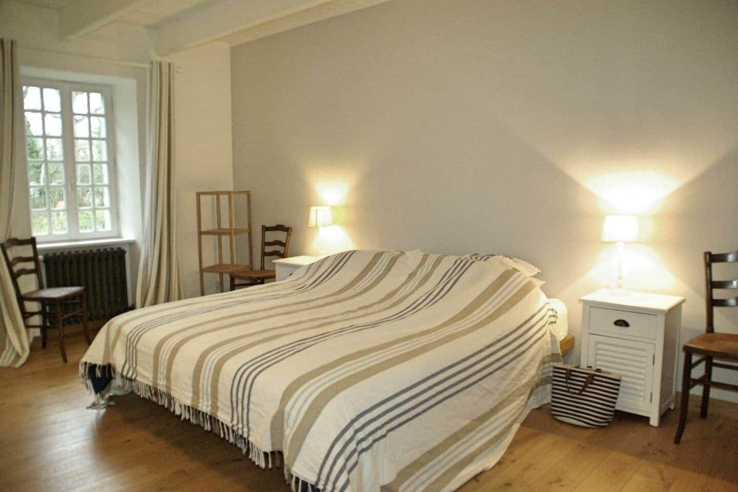 A bedroom with a bed, two bedside tables, a chair, a radiator, and a window.
