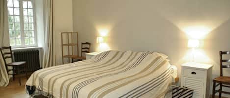 A bedroom with a bed, two bedside tables, a chair, a radiator, and a window.