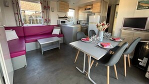 Ett kompakt bostadsutrymme med en soffa, ett matbord, stolar, ett litet kök och en tv.