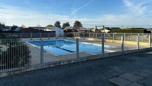 En rektangulär swimmingpool omgiven av ett staket av metall, med en klarblå himmel ovanför.