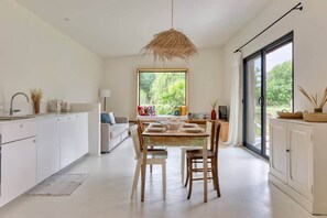 Cozinha moderna com armários brancos, uma mesa de jantar posta para dois e uma grande janela com vista para o verde lá fora.