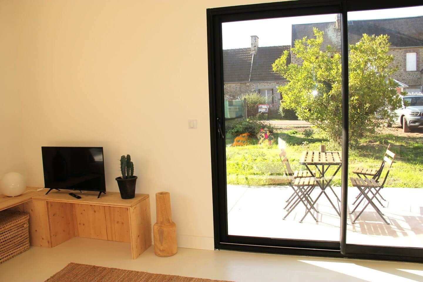 Ein Zimmer mit Fernseher auf einem Holzständer, einem Topf mit einem Kaktus und einer Schiebetür zu einer Außenpatio mit Tisch und Stühlen.