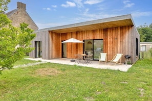 Ein modernes Haus mit Holzfassade, einer Terrasse und Gartenmöbeln sowie einer großen Glasdoor.