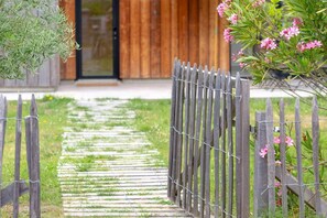 A wooden fence with a gate, a stone pathway, and a wooden building in the background. - Casa ZaO Jolie maison en bois brut de 50m2 à (Gouville-sur-Mer)