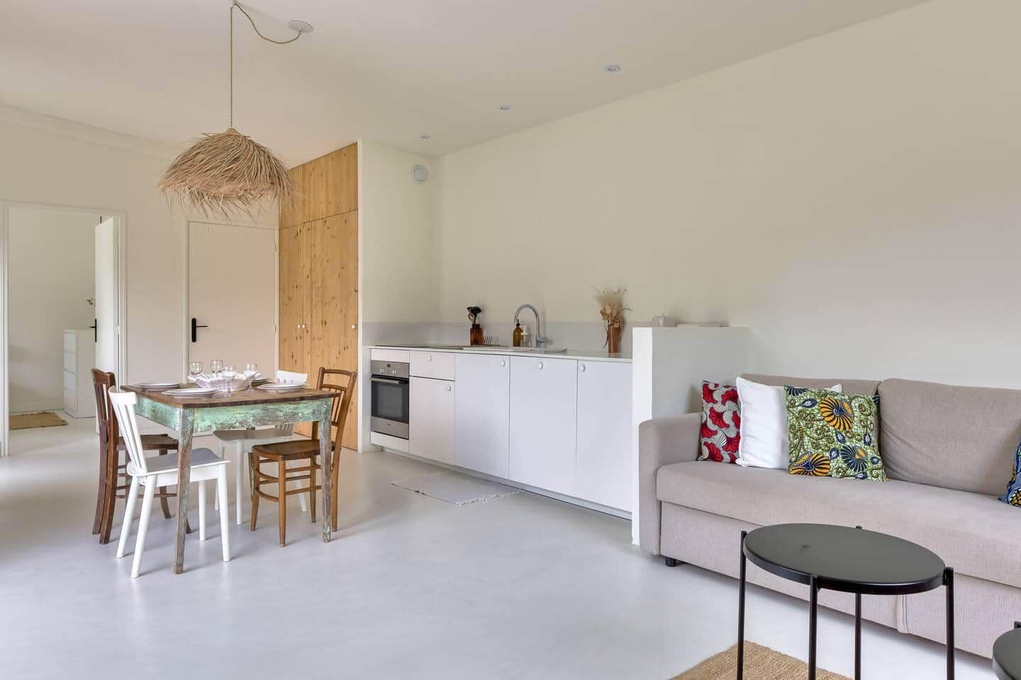 A modern kitchen with white cabinets, a dining table with chairs, a sofa, and a small round table.