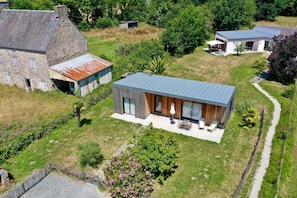 A modern house with a large patio, surrounded by a well-maintained lawn and trees. - Casa ZaO Jolie maison en bois brut de 50m2 à (Gouville-sur-Mer)