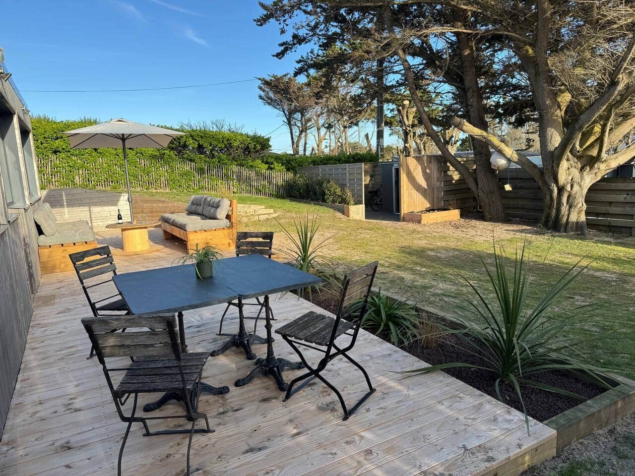 An outdoor patio with a table and chairs, surrounded by a wooden deck and a grassy area with trees.