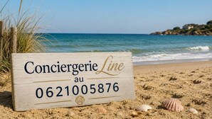 Un senyal de fusta amb la inscripció 'Conciererie Line au 0621005876' a una platja de sorra i petxines.