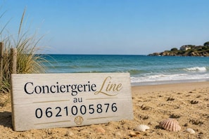 A wooden sign with 'Conciererie Line au 0621005876' on a beach with sand and shells. - La Perle des Dunes-Seafront-Direct beach access (Montmartin-sur-Mer)