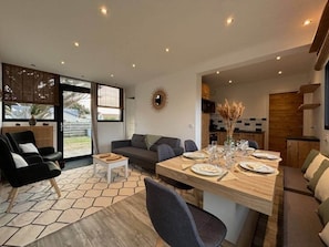 A modern living room with a dining area, a sofa, a coffee table, and a kitchen visible in the background. - La Perle des Dunes-Seafront-Direct beach access (Montmartin-sur-Mer)