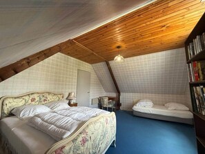 Ein Schlafzimmer mit schrägem Dach, einem Bett, einem Nachttisch, einem Sessel und einem Bücherregal.