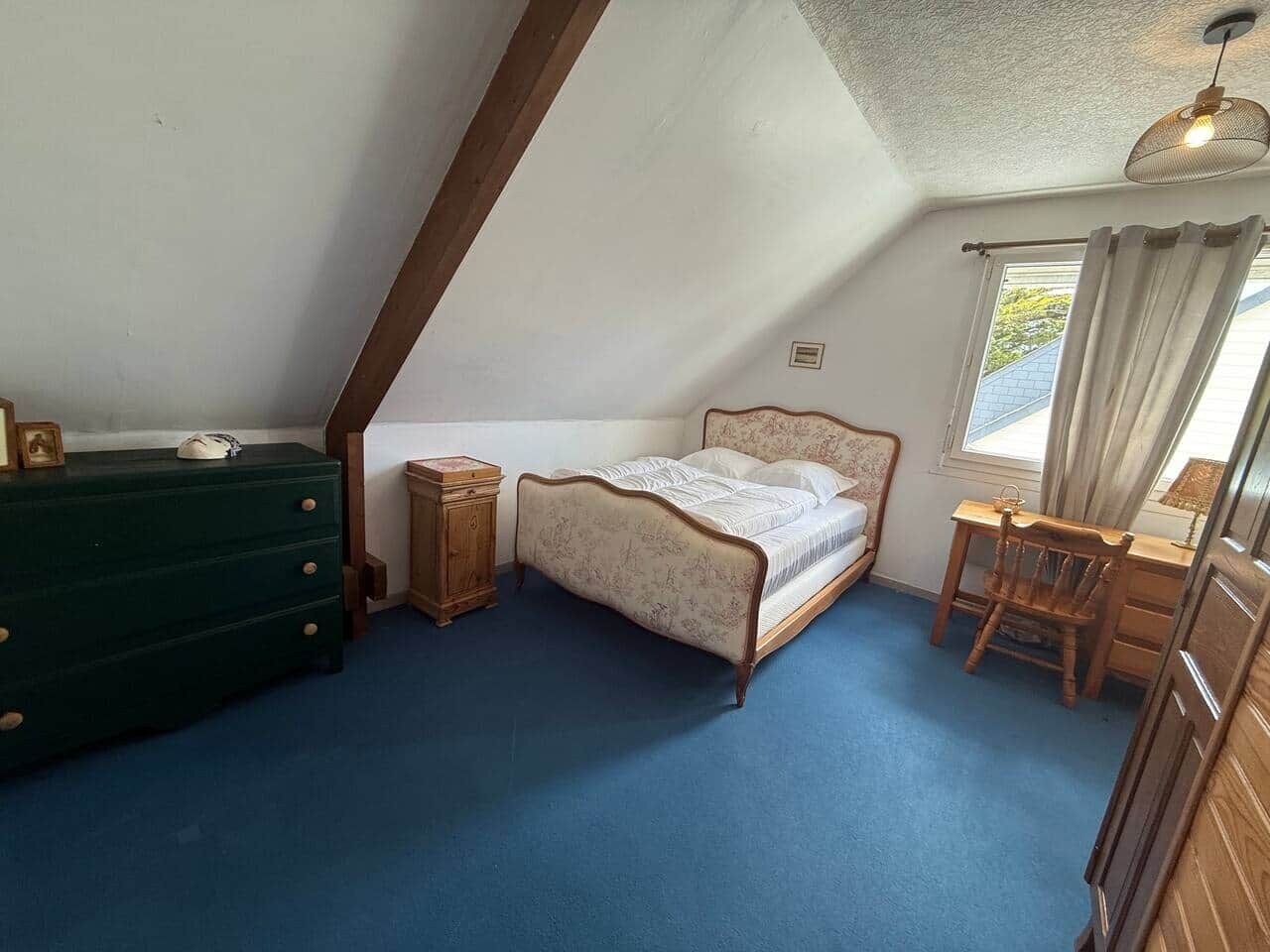 Une chambre avec un plafond en pente, un lit, une commode, une table de chevet et un bureau avec une chaise.