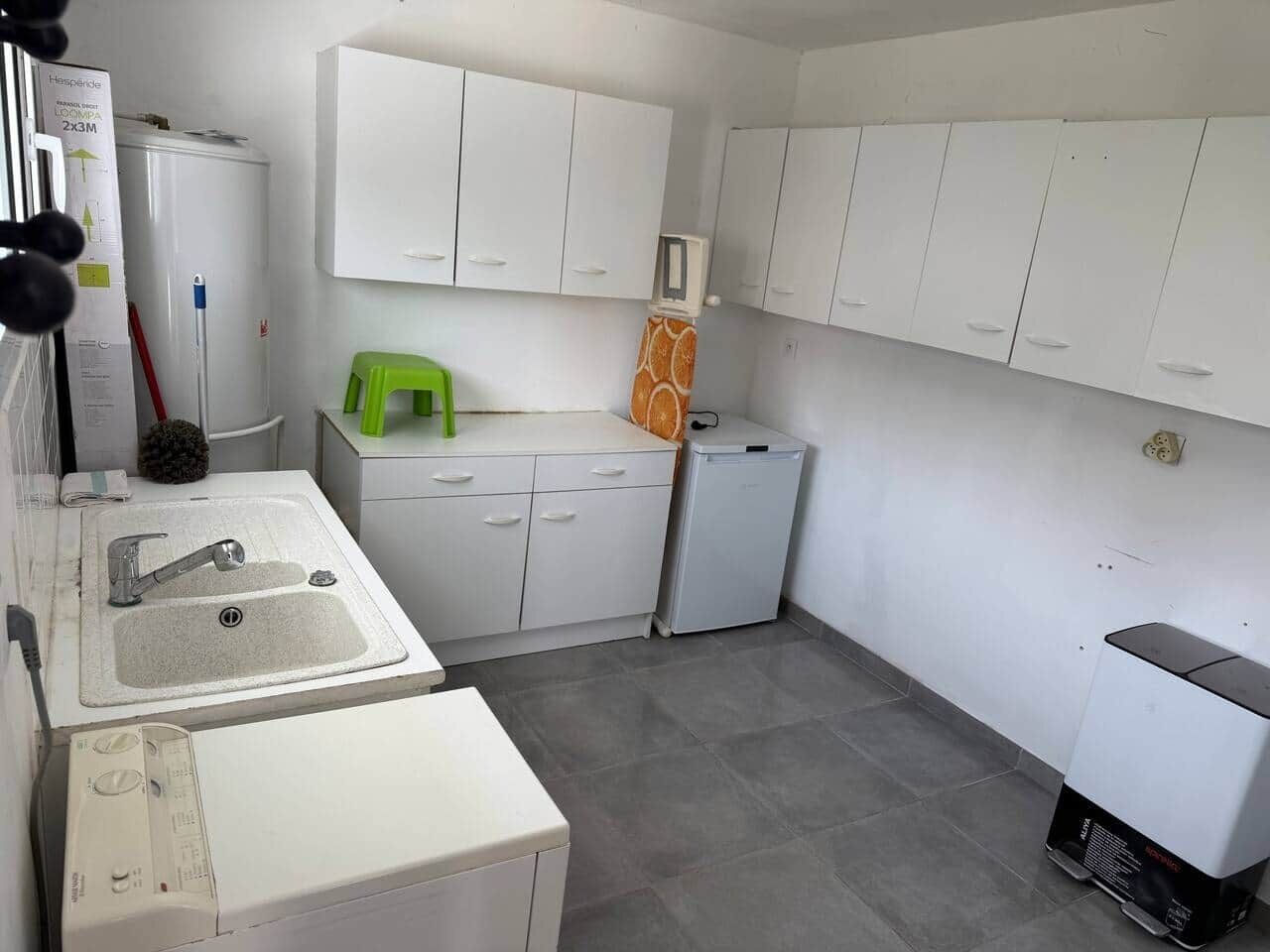 Uma cozinha compacta com pia, armários, um banquinho verde e uma geladeira compacta.
