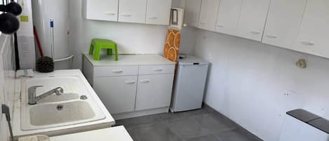 Uma cozinha compacta com pia, armários, um banquinho verde e uma geladeira compacta.