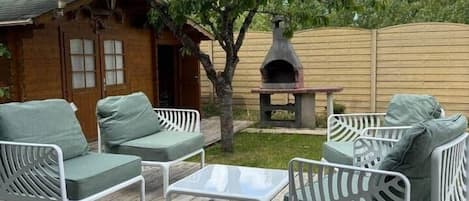 Una terraza de madera con mobiliario exterior, un árbol y una zona de barbacoa.