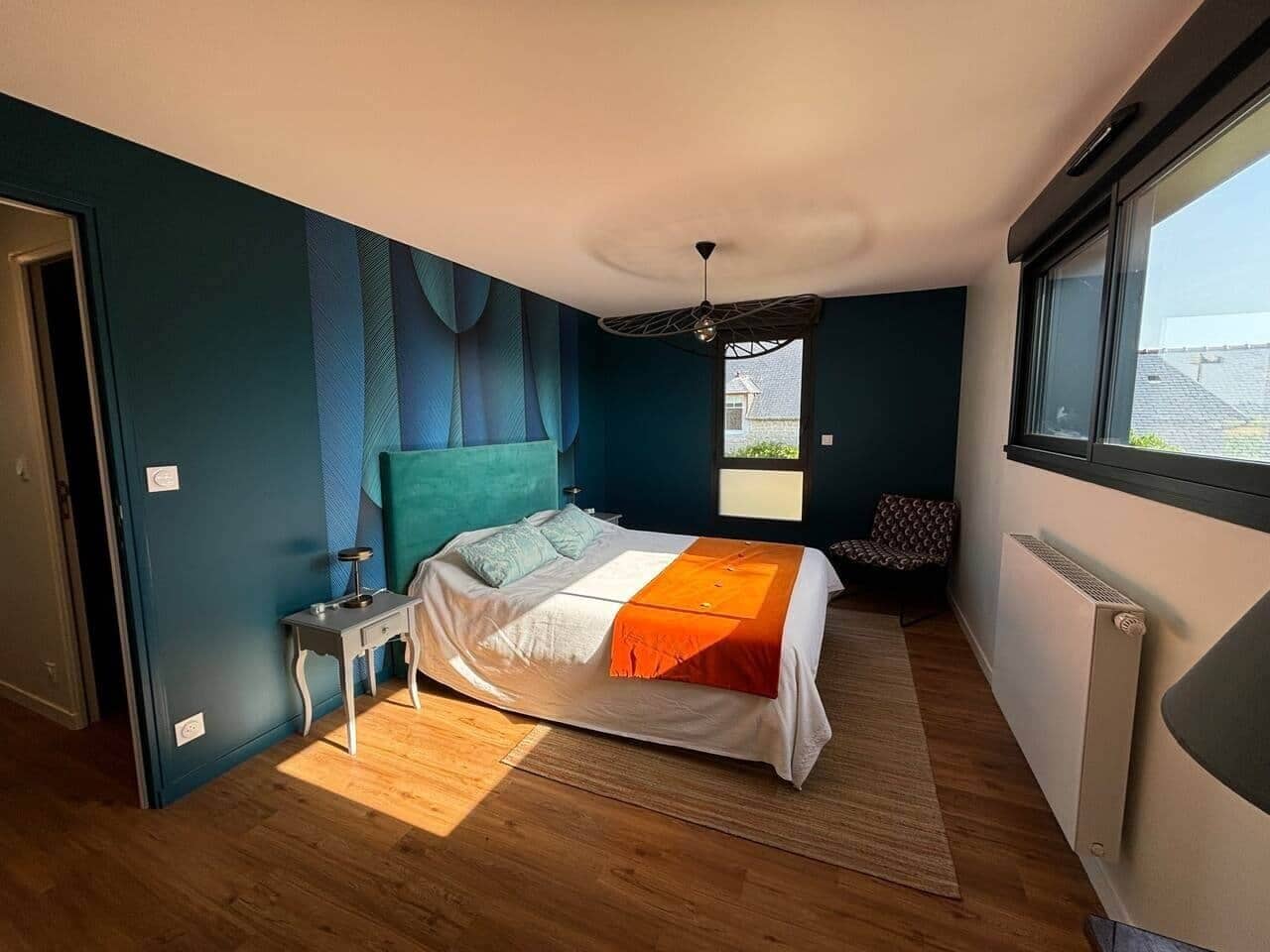 A bedroom with a bed, a nightstand, a window, and a radiator.