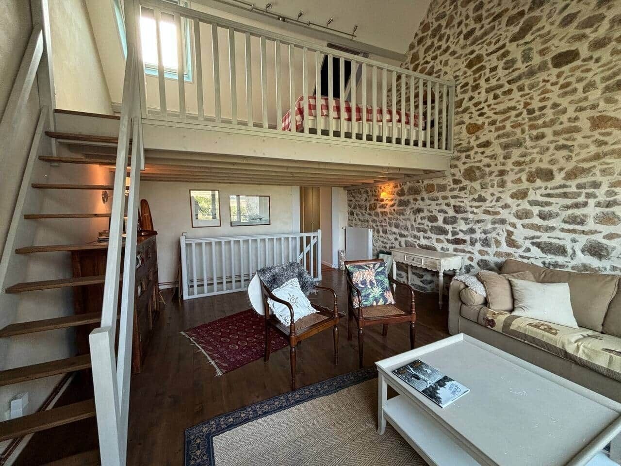 Un espace de vie de style industriel, avec un mur en pierre, un escalier en bois et un plafond haut.