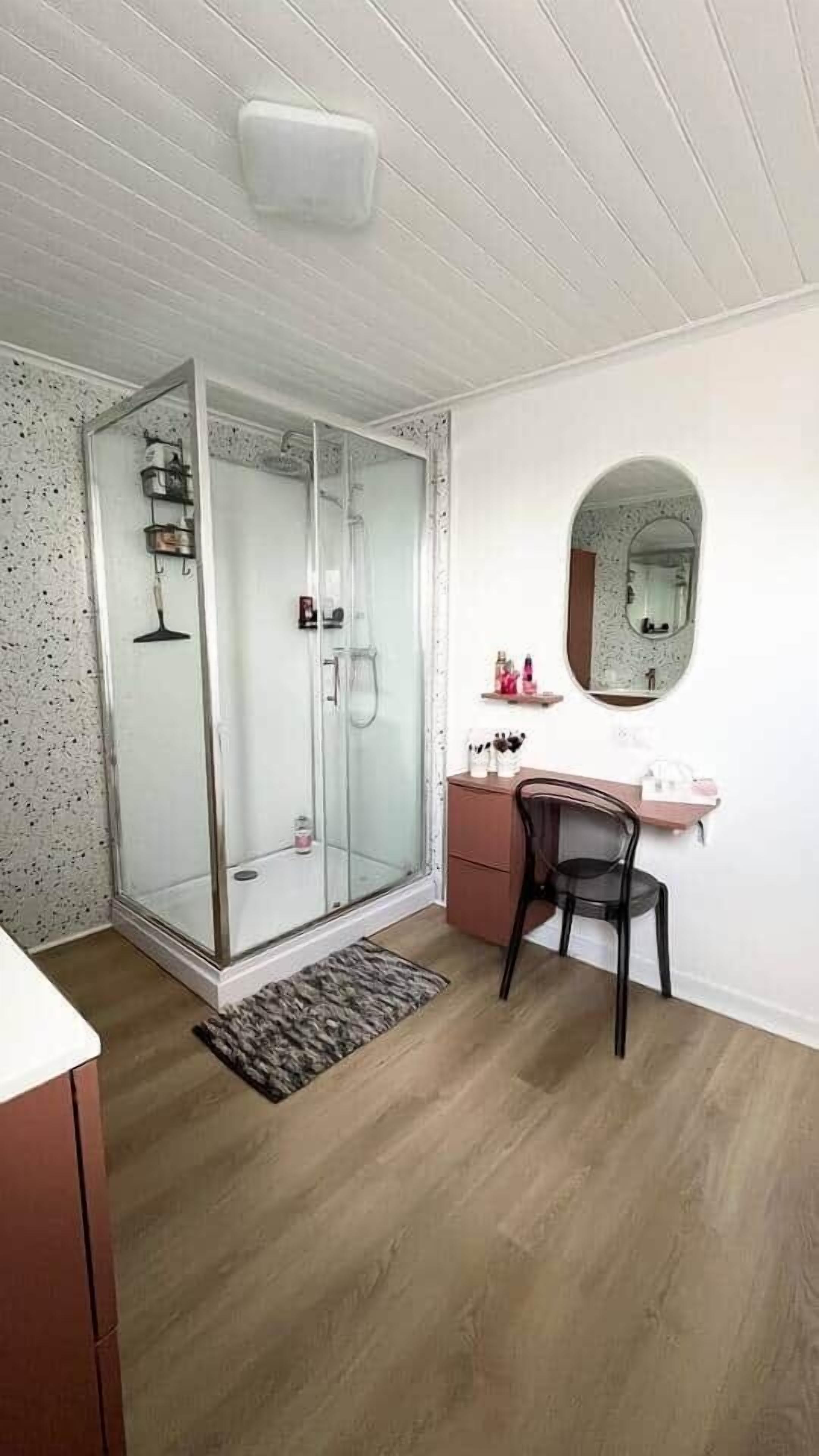 Een badkamer met een douchecabine van glas, een wastafel met spiegel en een stoel.