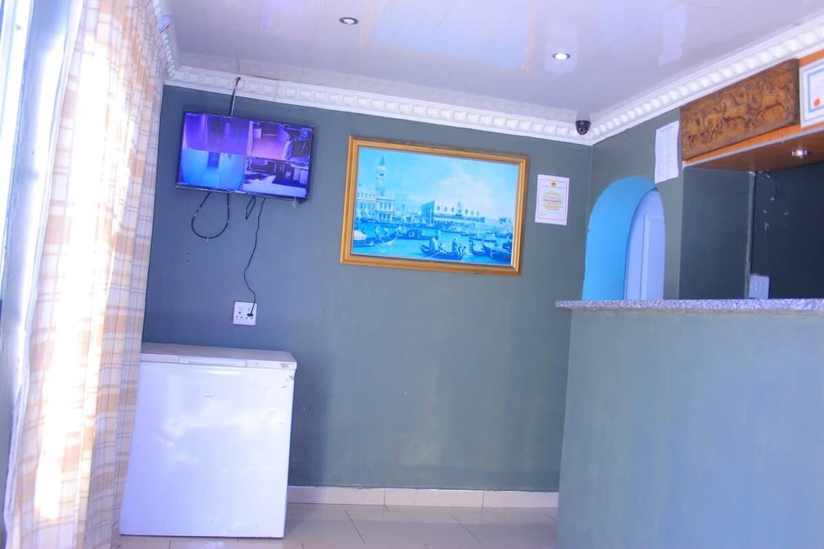 A room with a television mounted on the wall, a framed picture of a cityscape, a white refrigerator, and a counter with a sink.