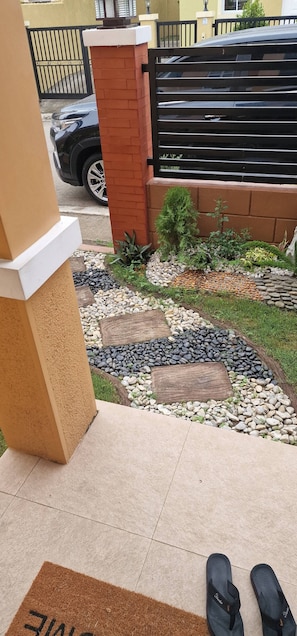 Un jardín con un felpudo, un coche negro estacionado afuera y una entrada con portón.