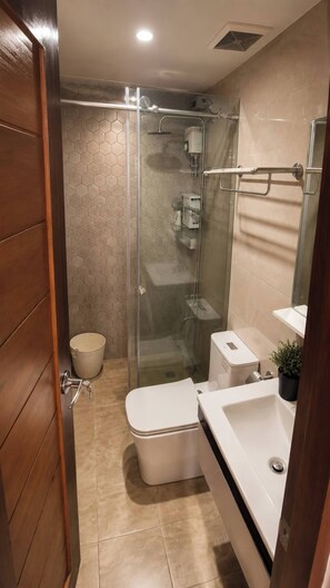 A modern bathroom with a glass-enclosed shower, a white toilet, and a sink with a mirror. - Nicholas Residence (Silang)