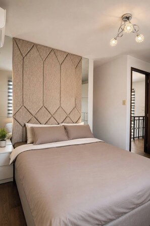 A bedroom with a large bed, a headboard with a geometric pattern, bedside tables, and a ceiling light fixture. - Nicholas Residence (Silang)