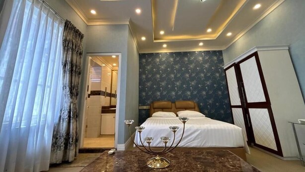 Quarto com cama, mesa de cabeceira, candelabro e janela com cortinas.