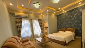 Quarto de hotel com cama, sofá, mesa de centro e lustre.