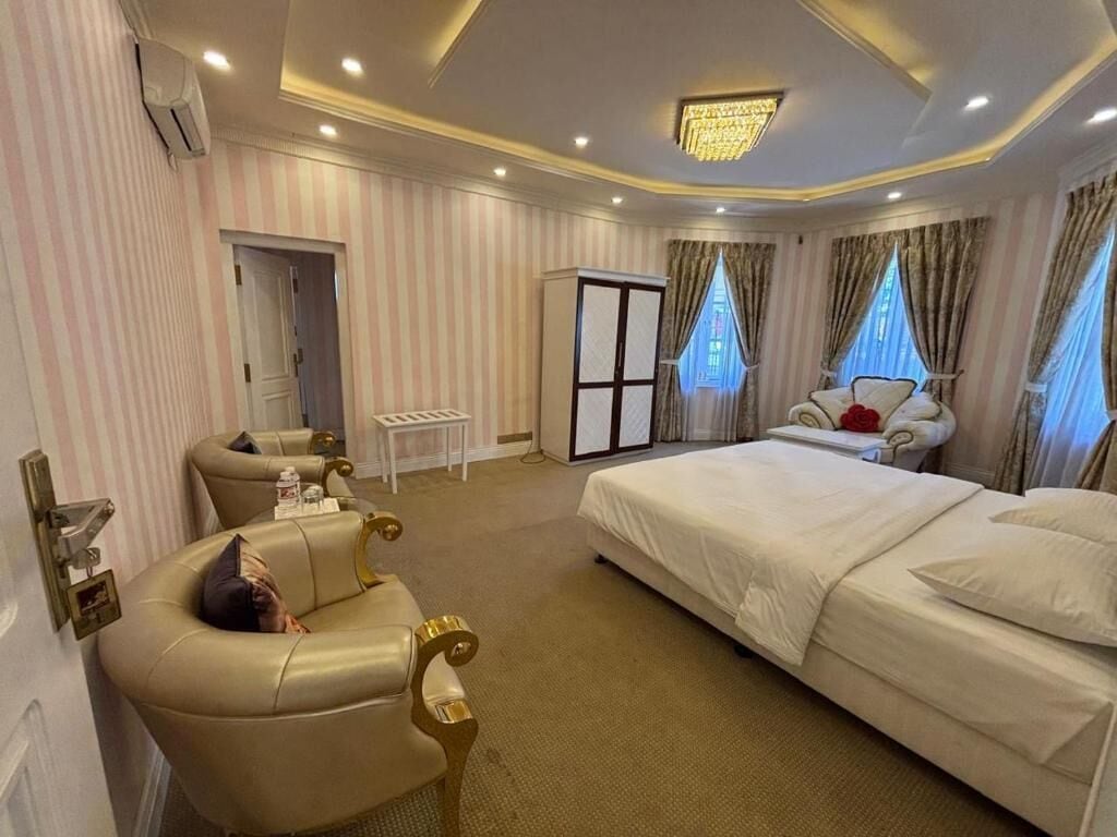 A hotel room with a large bed, a sitting area with a chair, a small table, and a wardrobe.