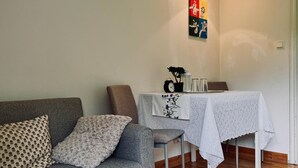 Ein Wohnzimmer mit grauem Sofa, einem kleinen Tisch mit weißem Tischtuch, einer Topfpflanze und Holzboden.