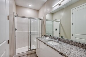A bathroom with a glass shower enclosure, a granite countertop sink, and a large mirror. - 5BR Disney villa • Pool • Themed rooms (Kissimmee)