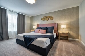 Ett hotellrum med en stor säng, två sängbord, en väggmonterad lampa och ett fönster med gardiner.