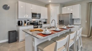 A modern kitchen with white cabinetry, stainless steel appliances, and a central island with seating. - 5BR Formosa Villa Near Disney | Private Pool (Kissimmee)