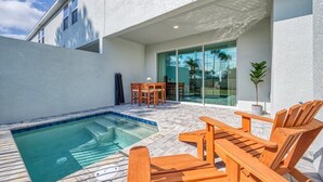 A swimming pool with wooden lounge chairs, a patio table, and a glass door leading to a covered area. - 5BR Formosa Villa Near Disney | Private Pool (Kissimmee)