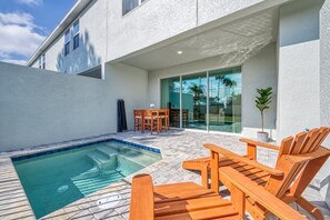 A swimming pool with wooden lounge chairs, a patio table, and a glass door leading to a covered area. - 5BR Formosa Villa Near Disney | Private Pool (Kissimmee)