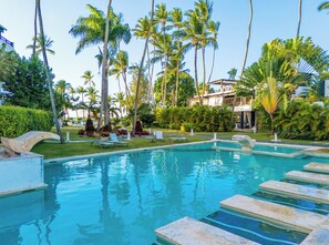 A swimming pool with lounge chairs, palm trees, and a building in the background. - Cozy 1-bedroom apartment jacuzzi Las Terrenas with AC (Las Terrenas)