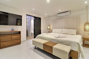 A modern bedroom with a large bed, a wooden dresser, a bench, a TV, and an air conditioning unit. - Cozy 1-bedroom apartment jacuzzi Las Terrenas with AC (Las Terrenas)