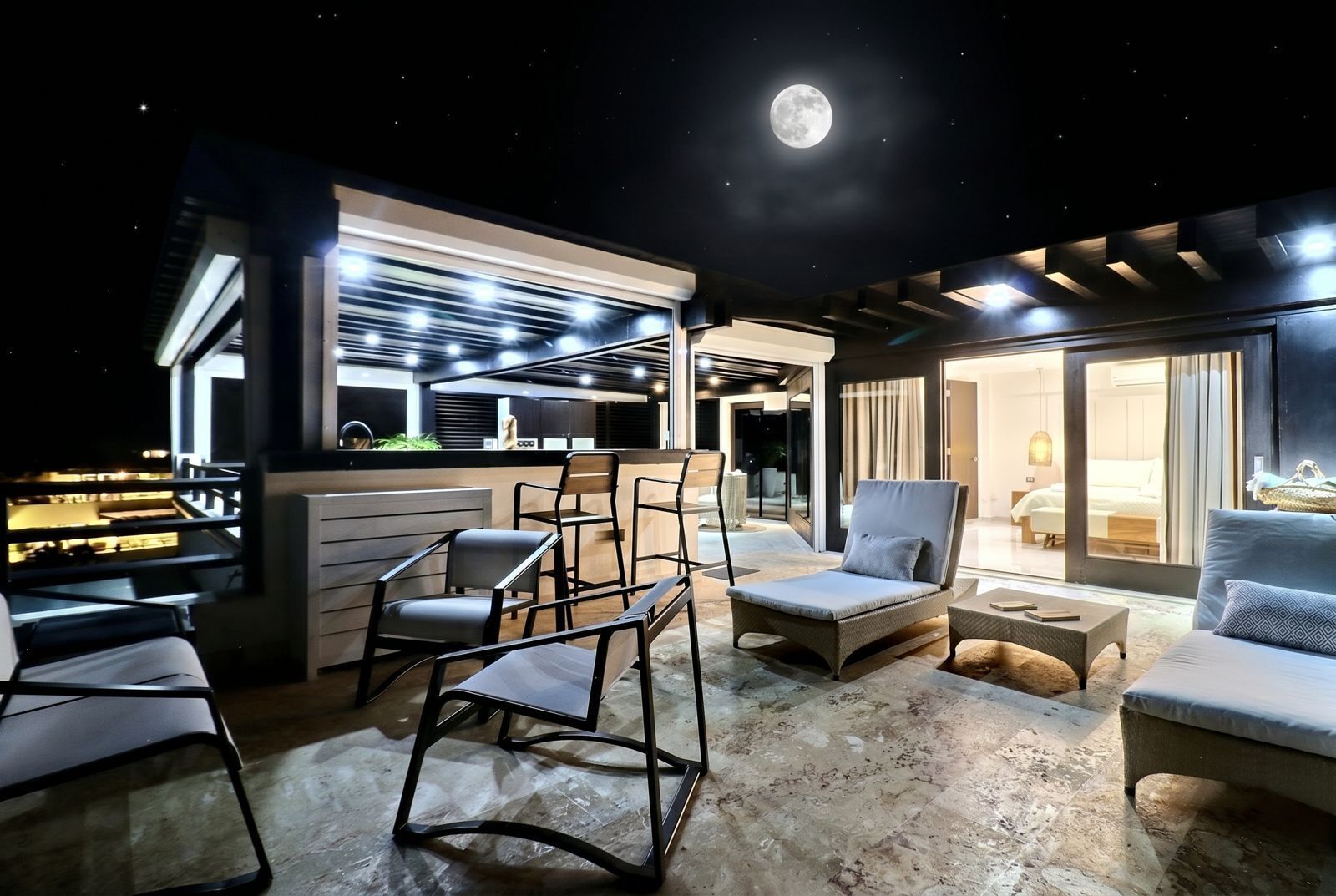 Un área lounge moderna al aire libre con asientos, un bar y vistas al cielo nocturno.