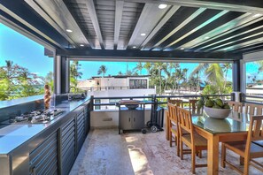 A modern kitchen with a glass-top table, wooden chairs, and a view of palm trees and buildings. - Cozy 1-bedroom apartment jacuzzi Las Terrenas with AC (Las Terrenas)