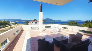 A balcony with outdoor furniture, a view of the sea, and distant mountains.