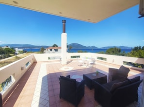 A balcony with outdoor furniture, a view of the sea, and distant mountains.