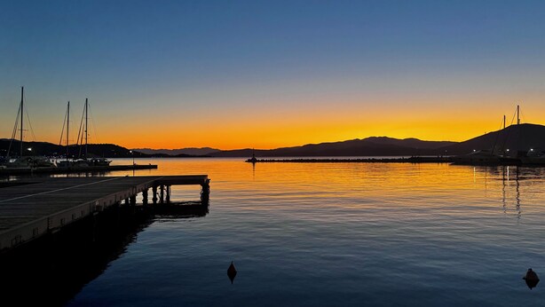 A marina with boats docked, calm water, and a sunset in the background.
